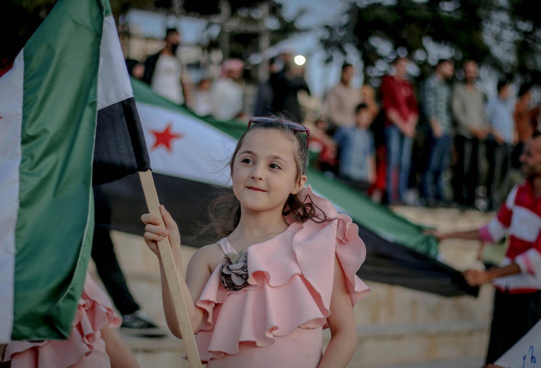 A girl smiling as she holds the Syrian independence flag at a celebration
